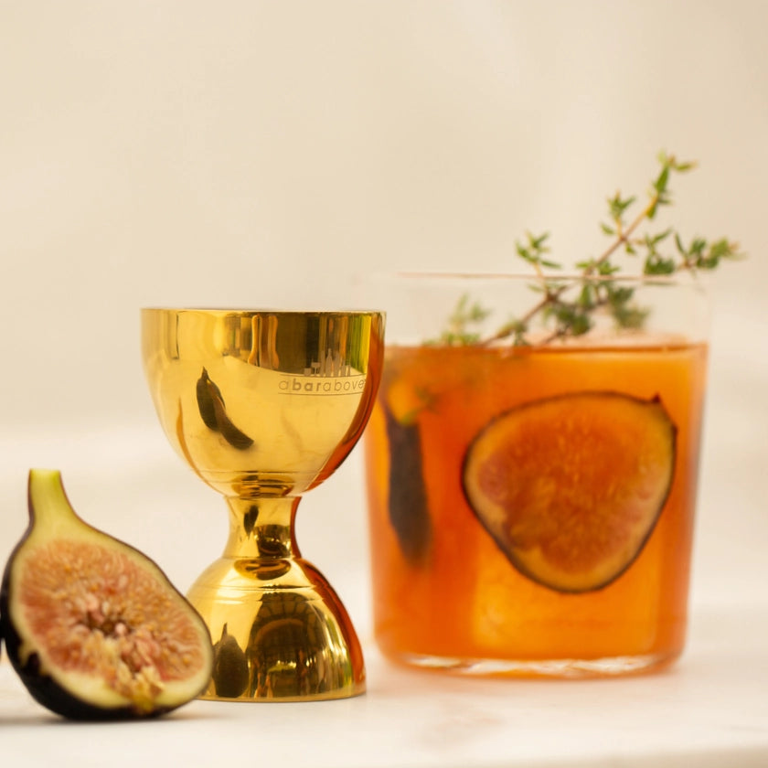Gold goblet and glass with fig and thyme garnish on a light background