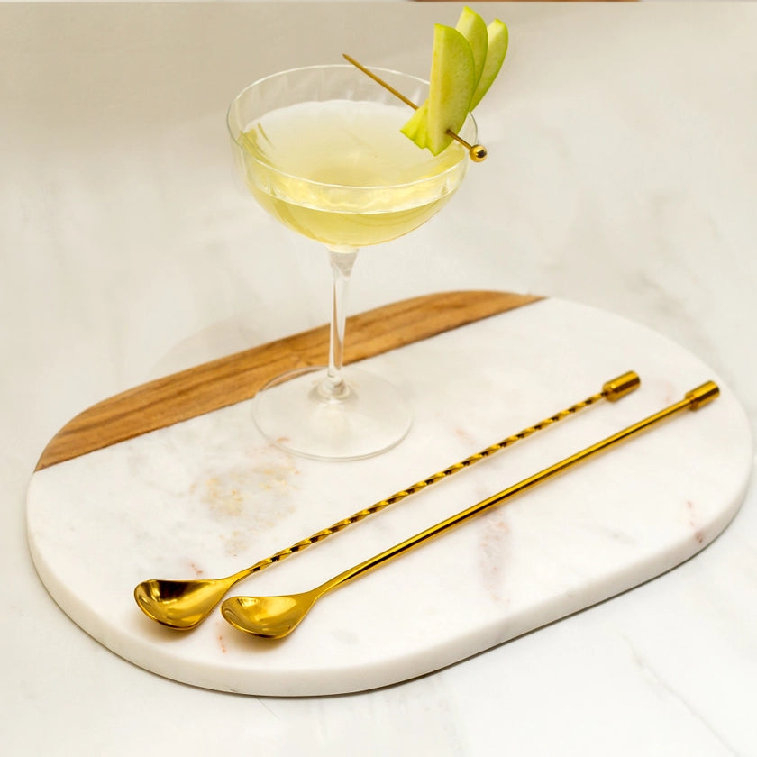 Cocktail with a garnish on a marble and wood board with gold straws.