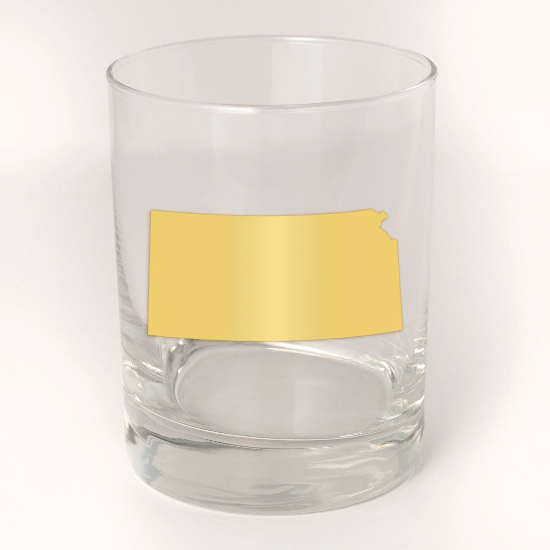 Clear glass tumbler with a gold Kansas-shaped decal on a white background