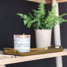 Candle labeled 'furnish' on a wooden tray with a plant in the background
